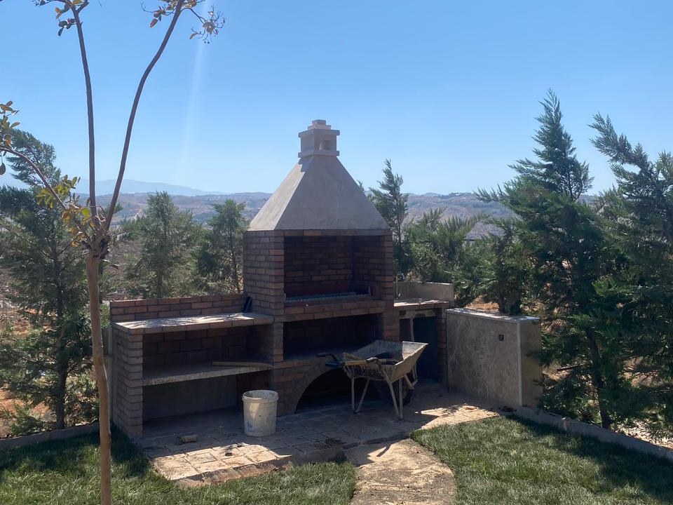 An outdoor brick barbecue and kitchen structure on a hilltop lawn, Machgara